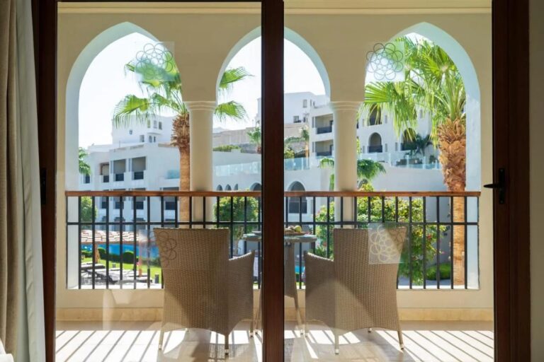 Un balcon à arcades avec deux fauteuils tressés, face aux palmiers et aux bâtiments blancs du Sunrise Arabian Beach Resort