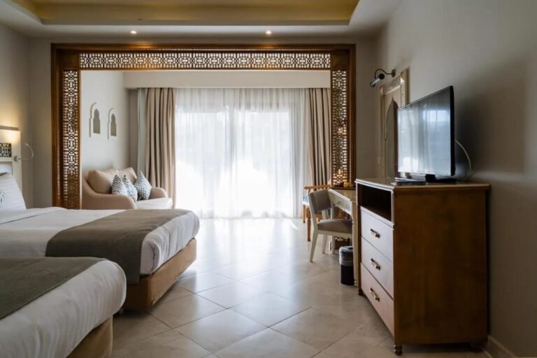 Une chambre à deux lits avec une commode, une télévision et un coin salon devant la baie vitrée