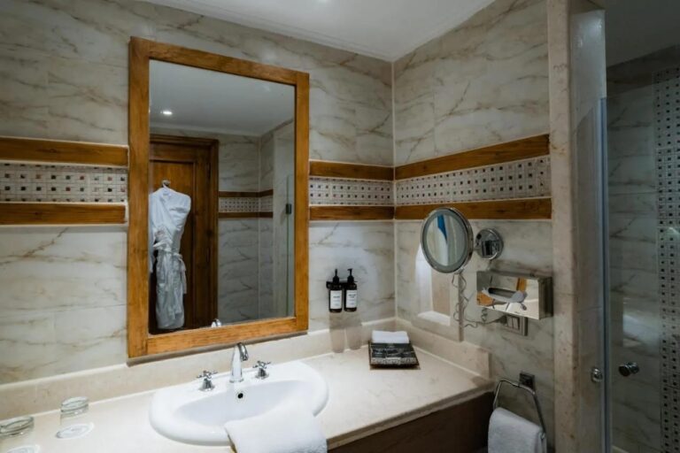 Une salle de bains avec vasque, miroir à cadre de bois clair et frise de mosaïque