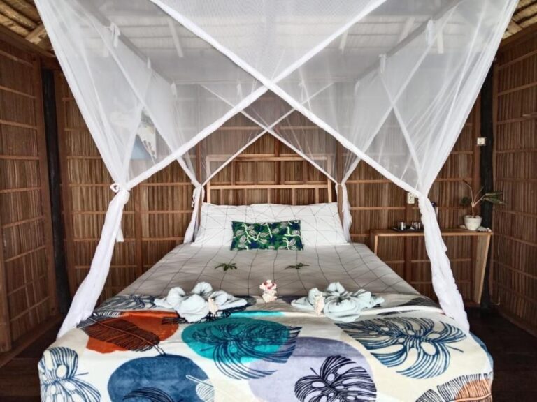 Un lit sous moustiquaire, avec un couvre-lit à feuilles bleues et des serviettes pliées