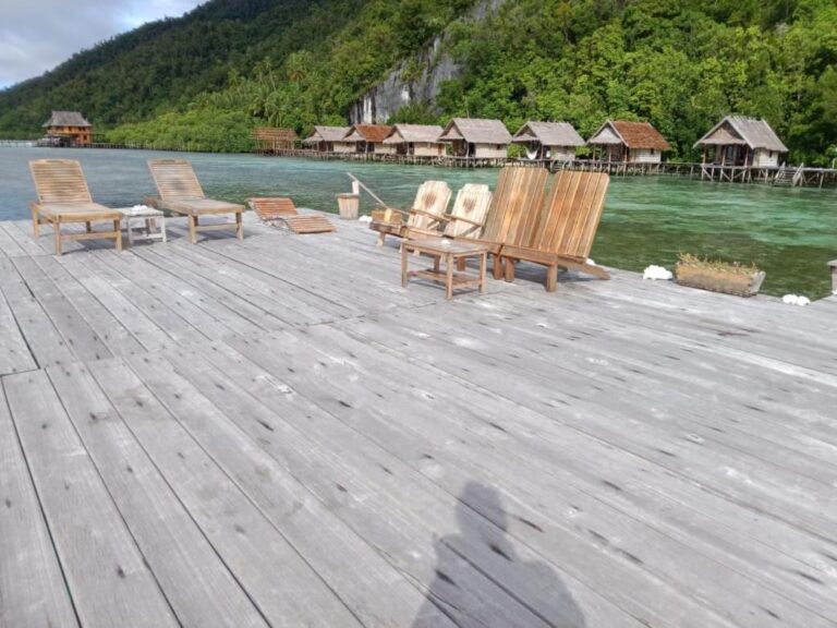 Un ponton en bois avec des chaises longues, face à la rangée de bungalows sur pilotis