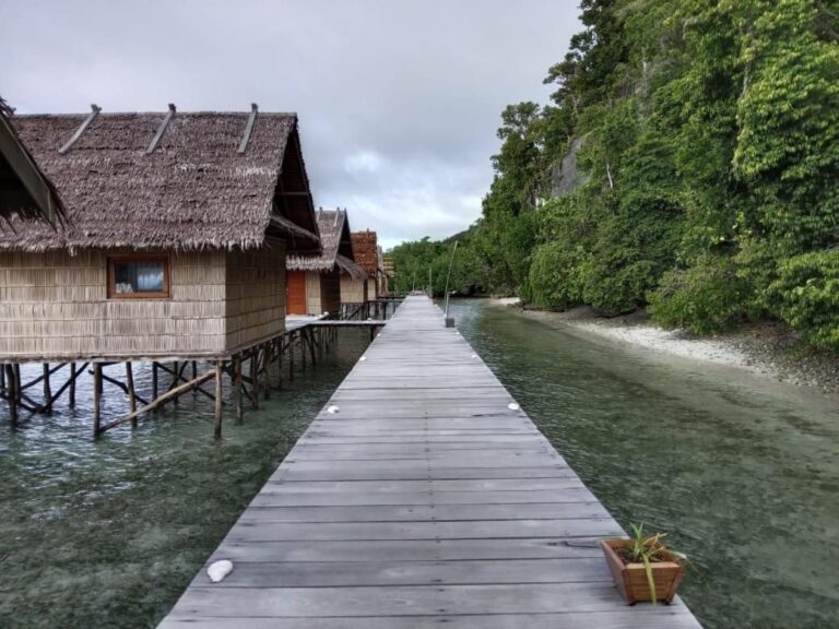 Une passerelle en bois au-dessus de l'eau, le long des bungalows aux toits de palmes