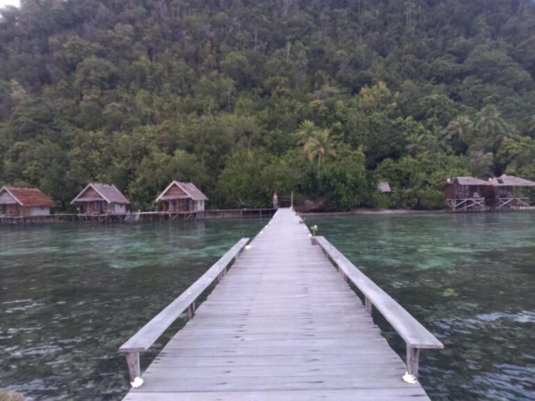 Un long ponton à bancs sur une eau calme, face aux bungalows et à la colline boisée