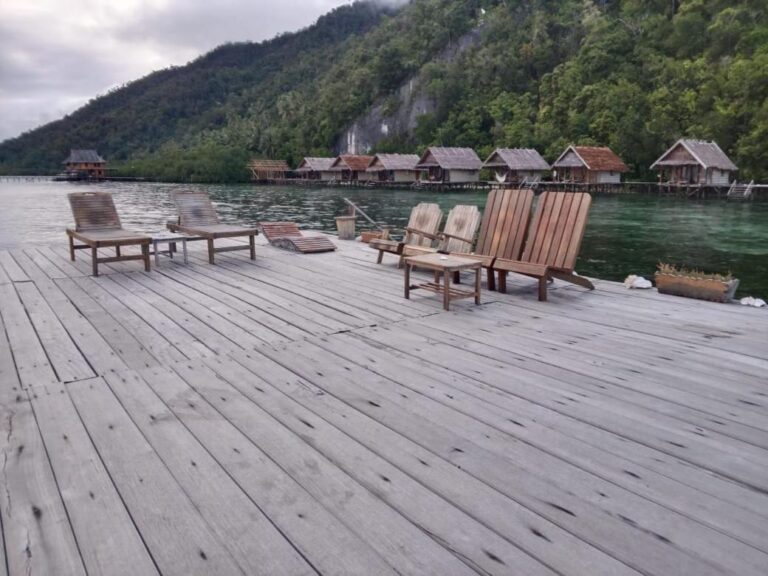 Des fauteuils en bois et une table basse sur un ponton, face à la falaise et à la forêt
