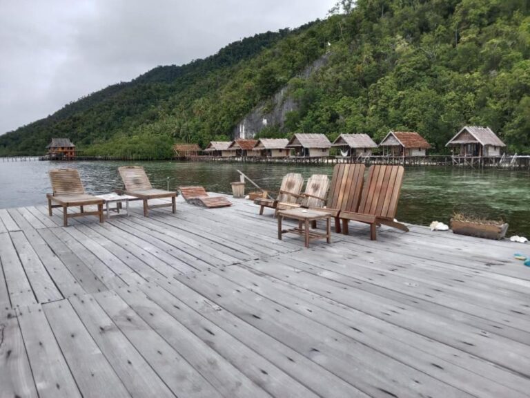 Des chaises longues sur un ponton par temps gris, devant les bungalows et la colline