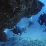 Quatre plongeurs sortent d'un tunnel de corail sur un fond de sable, à Cozumel, le plafond rocheux au-dessus d'eux