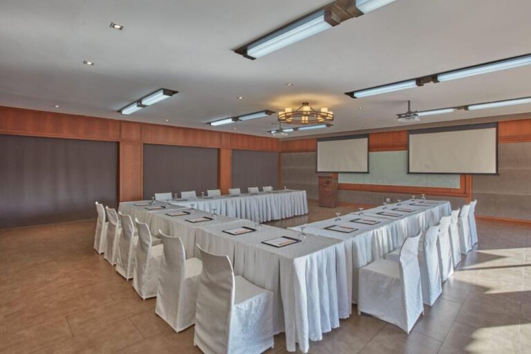 Une salle de réunion avec des tables en U nappées de blanc et deux écrans de projection