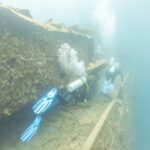 Deux plongeurs longent le pont du Thistlegorm le long d'une coursive, dans une eau bleu laiteux