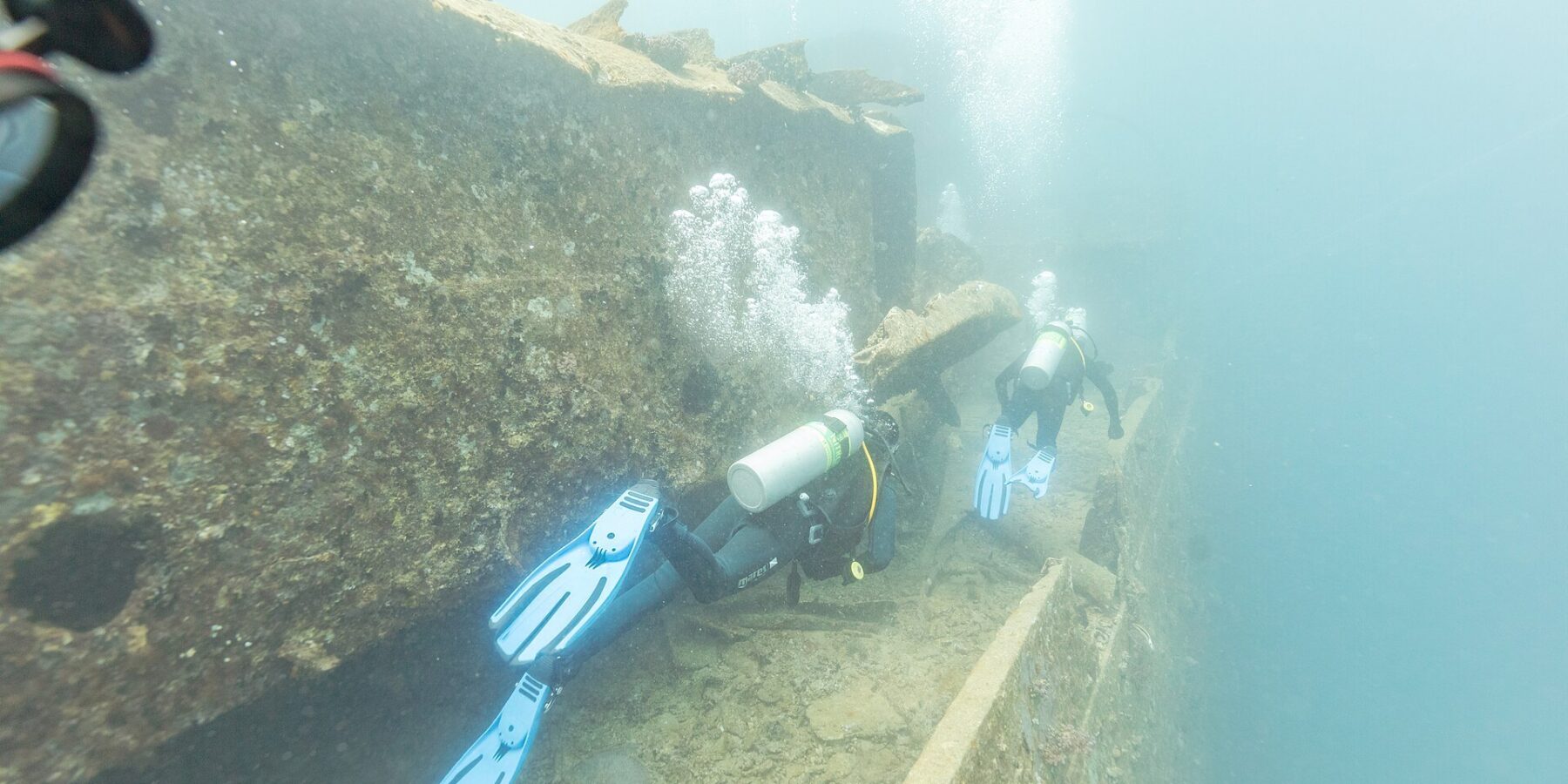 Deux plongeurs longent le pont du Thistlegorm le long d'une coursive, dans une eau bleu laiteux