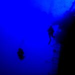 Dans un bleu profond, deux plongeurs en silhouette longent la rambarde de la poupe du Salem Express, le pont incliné à droite