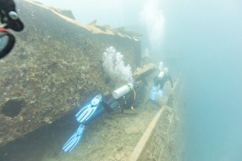 Deux plongeurs longent le pont du Thistlegorm le long d'une coursive, dans une eau bleu laiteux
