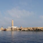Big Brother vue de la mer : un îlot plat et clair surmonté de son phare, un bateau de croisière blanc amarré devant