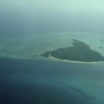 L'île de Misali vue d'avion, triangle de forêt bordé d'une plage blanche, posé sur un platier turquoise au milieu d'une mer bleu sombre, dans la brume